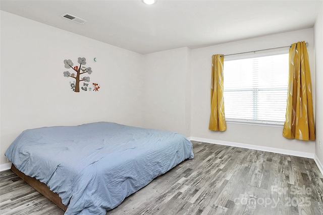 bedroom with baseboards, visible vents, and wood finished floors