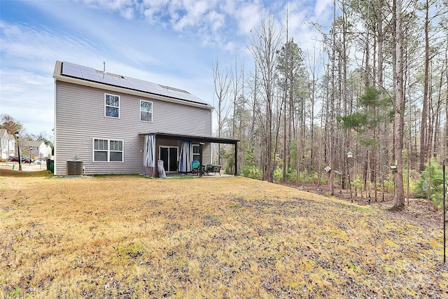 rear view of house with cooling unit, a lawn, and solar panels