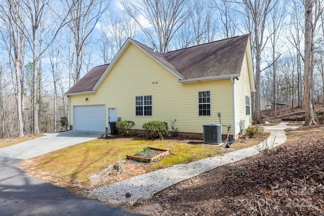 view of side of home featuring a garage, central AC, a garden, driveway, and roof with shingles