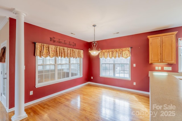 unfurnished dining area featuring visible vents, baseboards, light wood-style flooring, and ornate columns