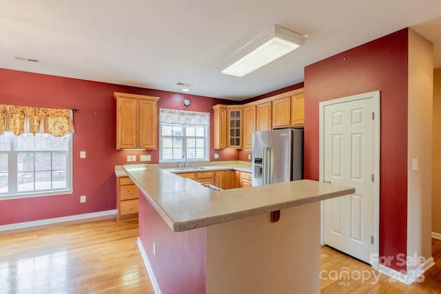 kitchen featuring light countertops, glass insert cabinets, light wood-style floors, high quality fridge, and a sink