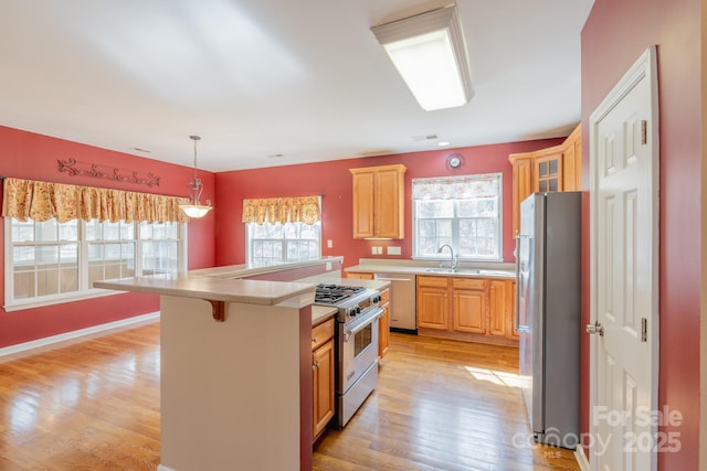 kitchen featuring a sink, light countertops, appliances with stainless steel finishes, light wood-type flooring, and decorative light fixtures