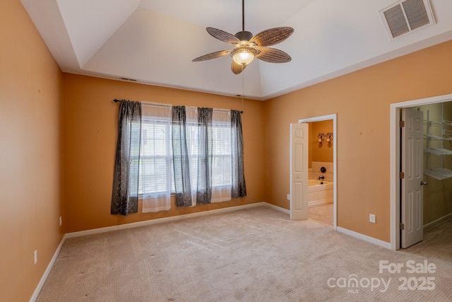 carpeted empty room featuring ceiling fan, visible vents, baseboards, vaulted ceiling, and a raised ceiling