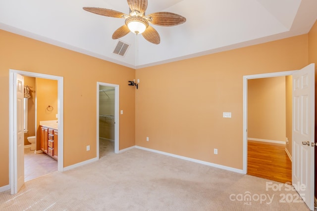 unfurnished bedroom with light carpet, visible vents, baseboards, ensuite bath, and a walk in closet