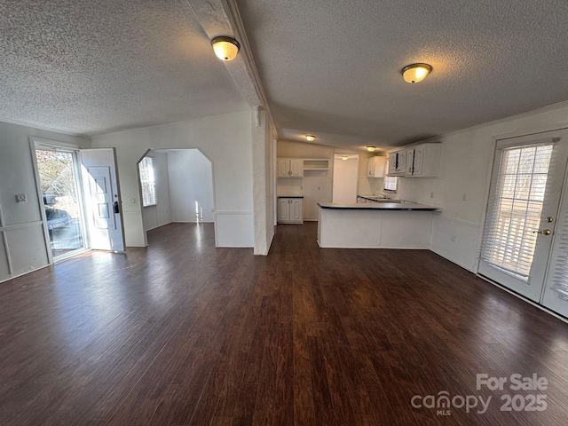 unfurnished living room featuring a wealth of natural light, arched walkways, dark wood finished floors, and a textured ceiling