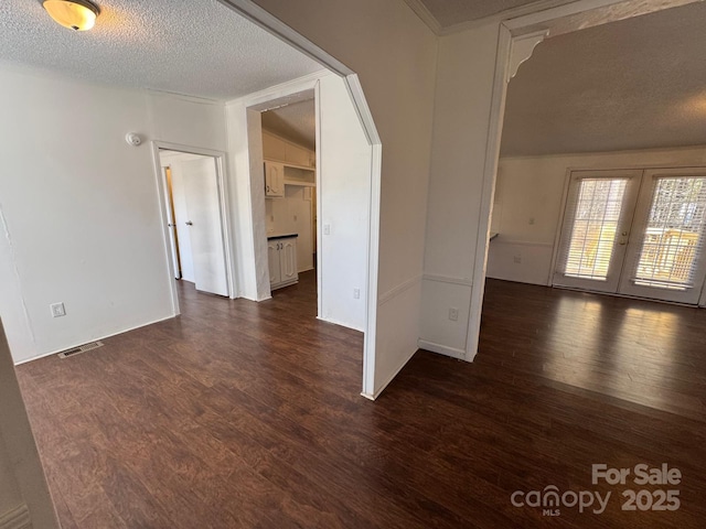 empty room featuring dark wood-style floors, french doors, a textured ceiling, and visible vents