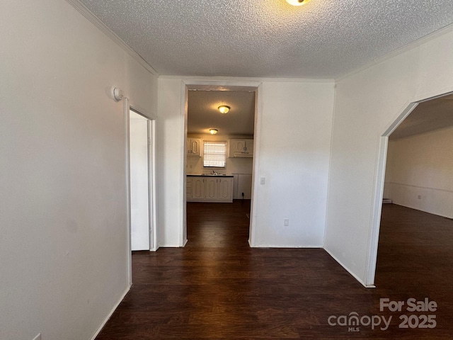 hallway with arched walkways, ornamental molding, a textured ceiling, and dark wood finished floors