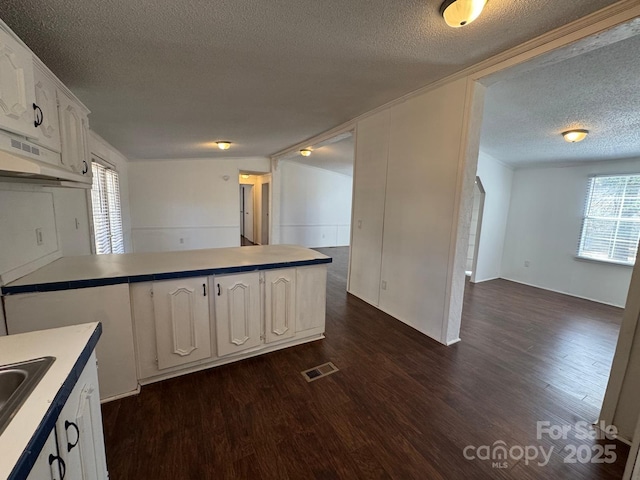 kitchen with a peninsula, visible vents, white cabinetry, and dark wood-style flooring