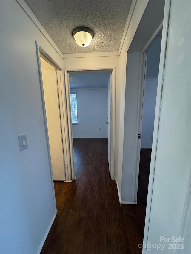 corridor with a textured ceiling, wood finished floors, and baseboards