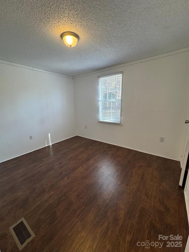 empty room featuring a textured ceiling, ornamental molding, dark wood-style flooring, and visible vents