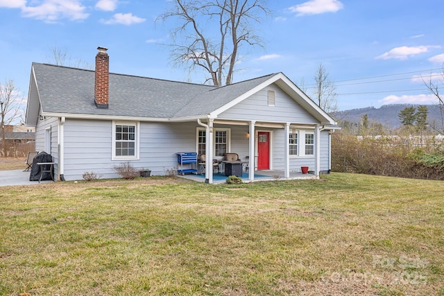 view of front of home featuring roof with shingles, a chimney, a front yard, a patio area, and a mountain view