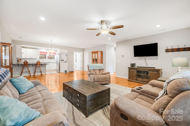 living area with light wood-type flooring, ceiling fan, baseboards, and recessed lighting