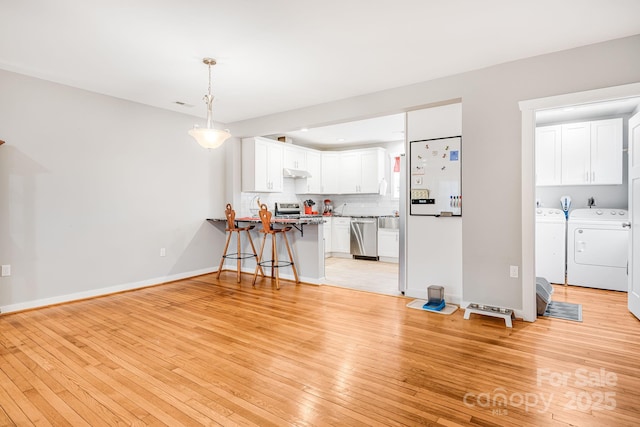 interior space with under cabinet range hood, stainless steel appliances, a breakfast bar, a peninsula, and separate washer and dryer