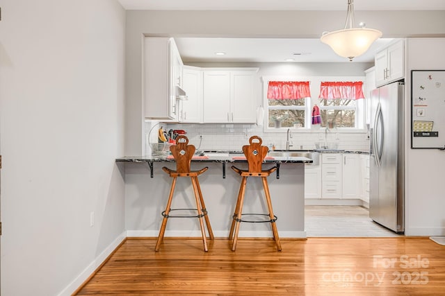 kitchen with a peninsula, a kitchen breakfast bar, light wood-type flooring, stainless steel fridge with ice dispenser, and tasteful backsplash