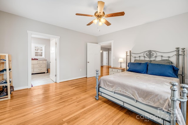 bedroom with light wood-style floors, ceiling fan, baseboards, and ensuite bathroom