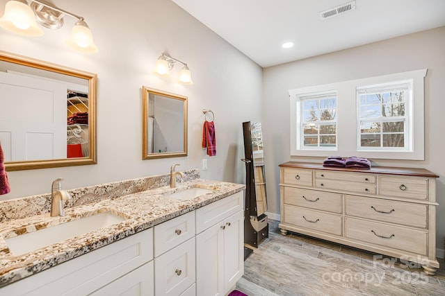 full bathroom with wood finished floors, visible vents, a sink, and double vanity