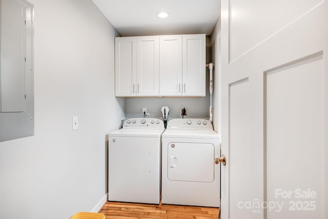 washroom featuring cabinet space, electric panel, baseboards, washer and clothes dryer, and light wood-type flooring