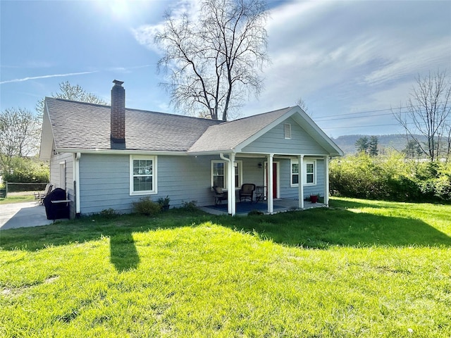 view of front of house featuring a patio area, roof with shingles, a chimney, and a front lawn