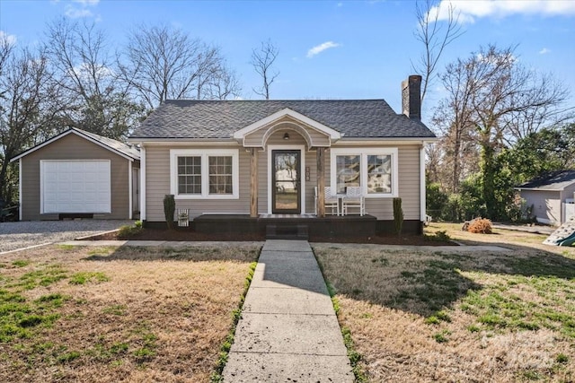 bungalow with an outbuilding, a detached garage, a chimney, a shingled roof, and a front yard