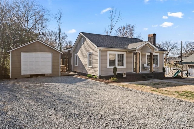 view of front facade featuring an outbuilding, a shingled roof, a detached garage, a chimney, and gravel driveway