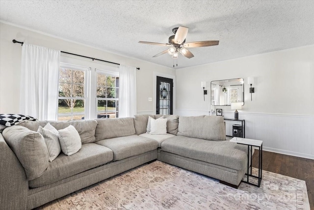 living area featuring a wainscoted wall, ceiling fan, a textured ceiling, and wood finished floors