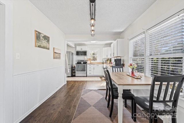 dining room featuring crown molding, a textured ceiling, dark wood-style flooring, and wainscoting