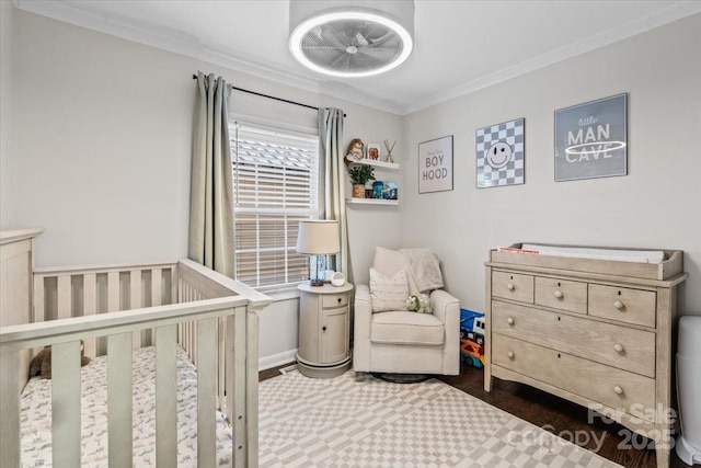 bedroom with dark wood-style floors, a crib, baseboards, and crown molding