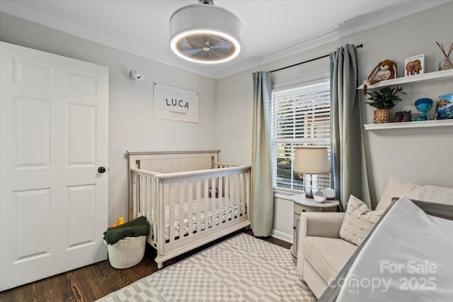 bedroom featuring a nursery area, ornamental molding, and wood finished floors