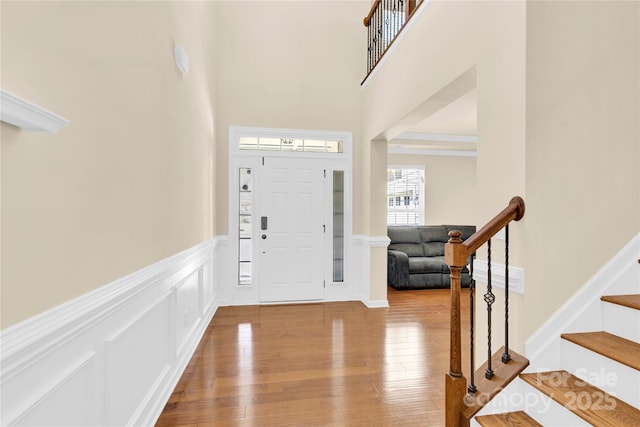 foyer with a decorative wall, a high ceiling, stairs, wainscoting, and hardwood / wood-style floors