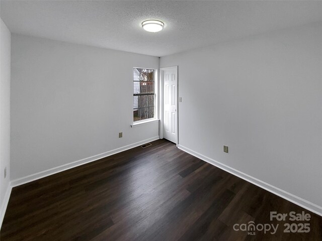 unfurnished room featuring dark wood-style floors, baseboards, visible vents, and a textured ceiling