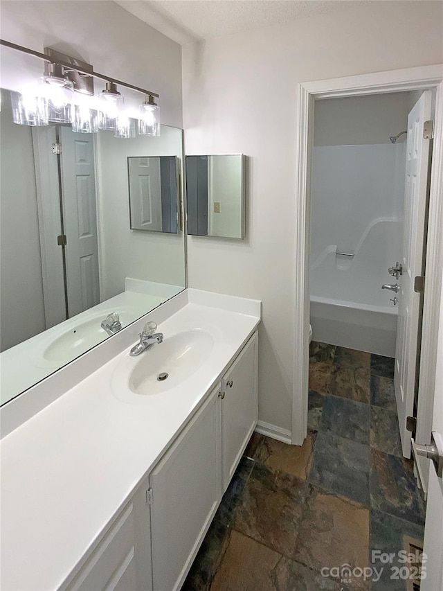 bathroom with toilet, vanity, baseboards, stone finish flooring, and washtub / shower combination