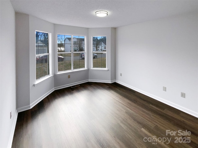 empty room with a textured ceiling, dark wood finished floors, visible vents, and baseboards