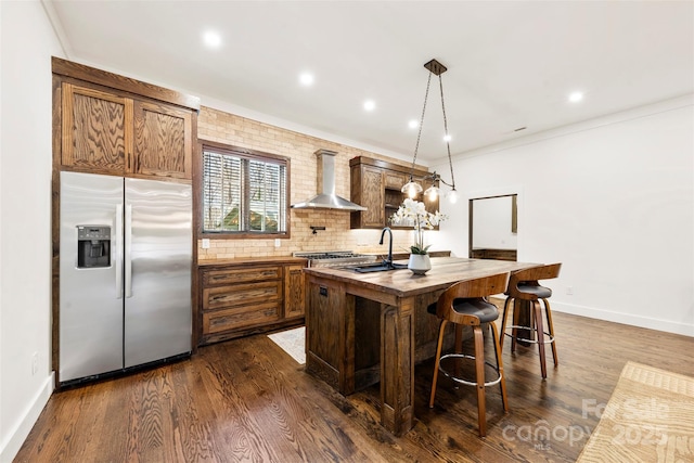 kitchen featuring wall chimney exhaust hood, a center island with sink, stainless steel refrigerator with ice dispenser, and dark wood-type flooring