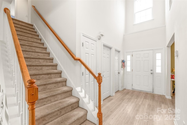 entrance foyer with light wood-type flooring, stairway, and a high ceiling