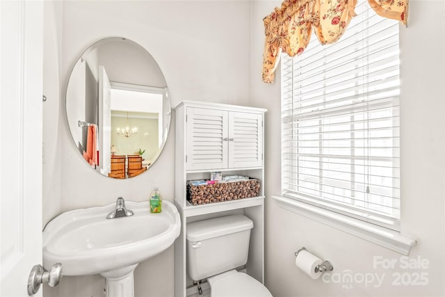 half bathroom with a sink, toilet, and a notable chandelier