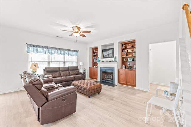 living room with light wood-type flooring, a fireplace with flush hearth, built in shelves, and ceiling fan