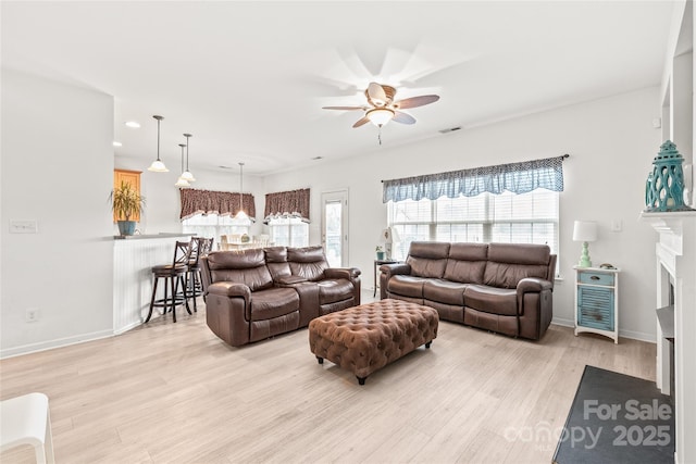 living area featuring visible vents, baseboards, ceiling fan, light wood-style floors, and a fireplace