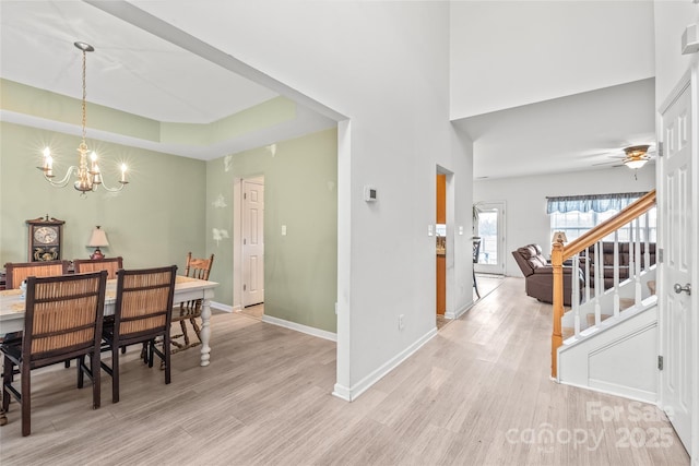 dining room featuring baseboards, a raised ceiling, light wood-style flooring, stairway, and ceiling fan with notable chandelier