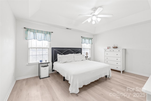 bedroom featuring light wood-style floors, a raised ceiling, visible vents, and baseboards