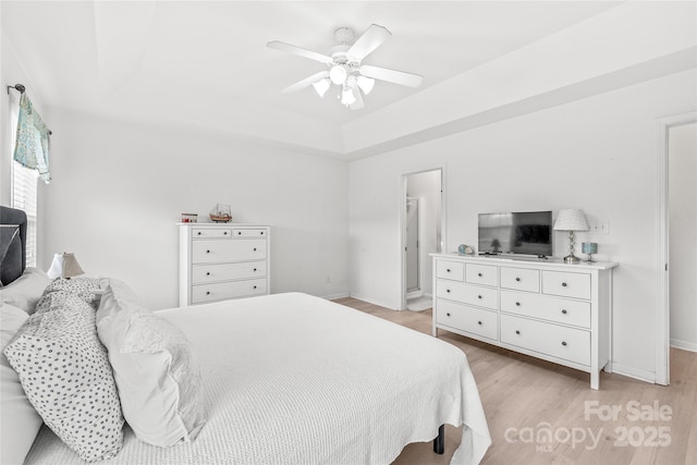 bedroom featuring light wood-style floors, baseboards, a tray ceiling, and a ceiling fan