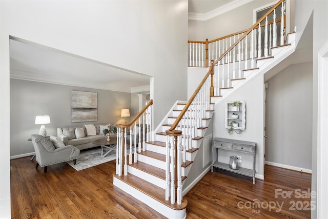 stairway with baseboards, a high ceiling, ornamental molding, and wood finished floors