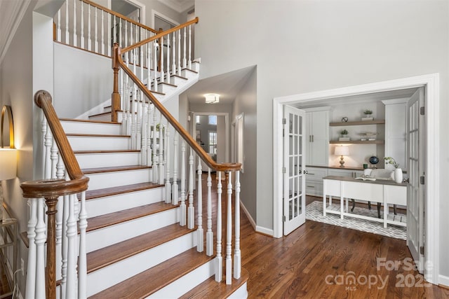 stairway featuring a towering ceiling, baseboards, and wood finished floors