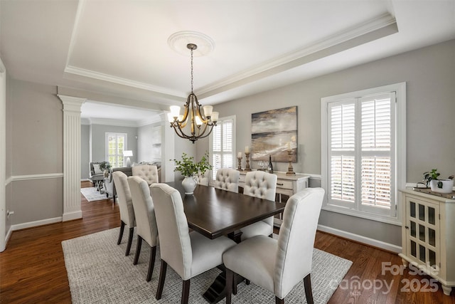 dining area featuring decorative columns, baseboards, a raised ceiling, wood finished floors, and a notable chandelier