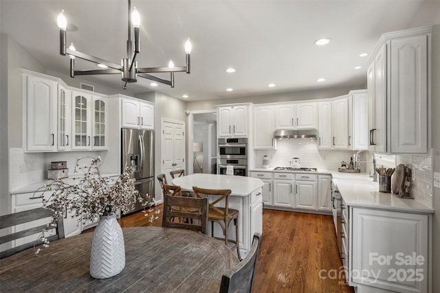 kitchen with appliances with stainless steel finishes, under cabinet range hood, a kitchen bar, white cabinetry, and a sink