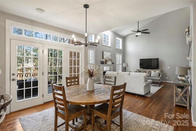 dining room featuring a fireplace, a towering ceiling, wood finished floors, baseboards, and ceiling fan with notable chandelier