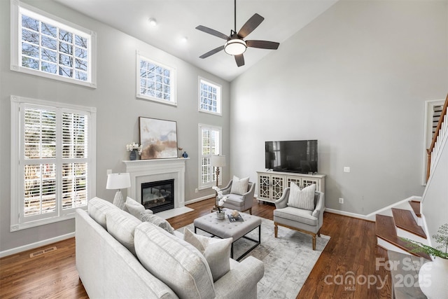 living room featuring baseboards, visible vents, a fireplace with flush hearth, stairway, and wood finished floors