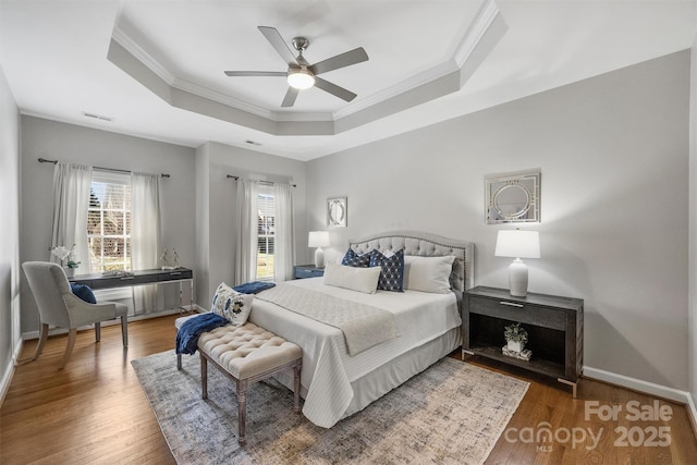 bedroom featuring baseboards, visible vents, a raised ceiling, wood finished floors, and crown molding