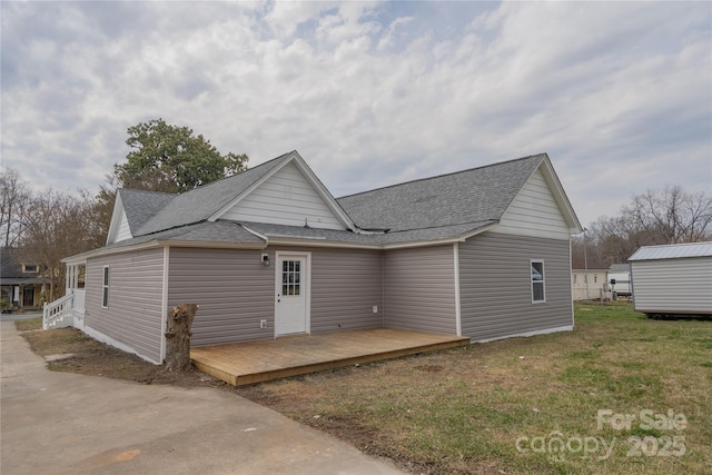 back of house with a deck, a yard, a shingled roof, and an outbuilding