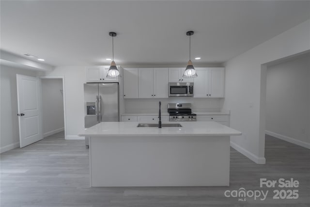 kitchen with stainless steel appliances, light countertops, light wood-style flooring, white cabinetry, and a sink