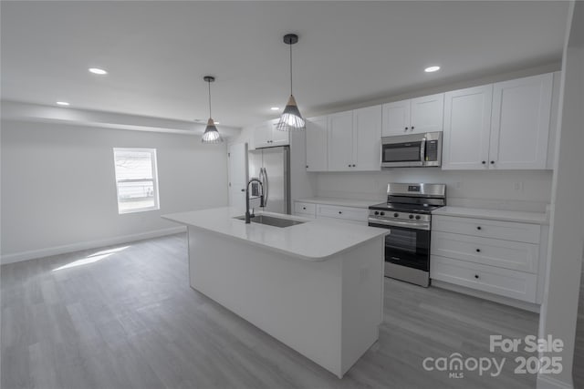 kitchen with stainless steel appliances, a sink, white cabinets, light countertops, and an island with sink